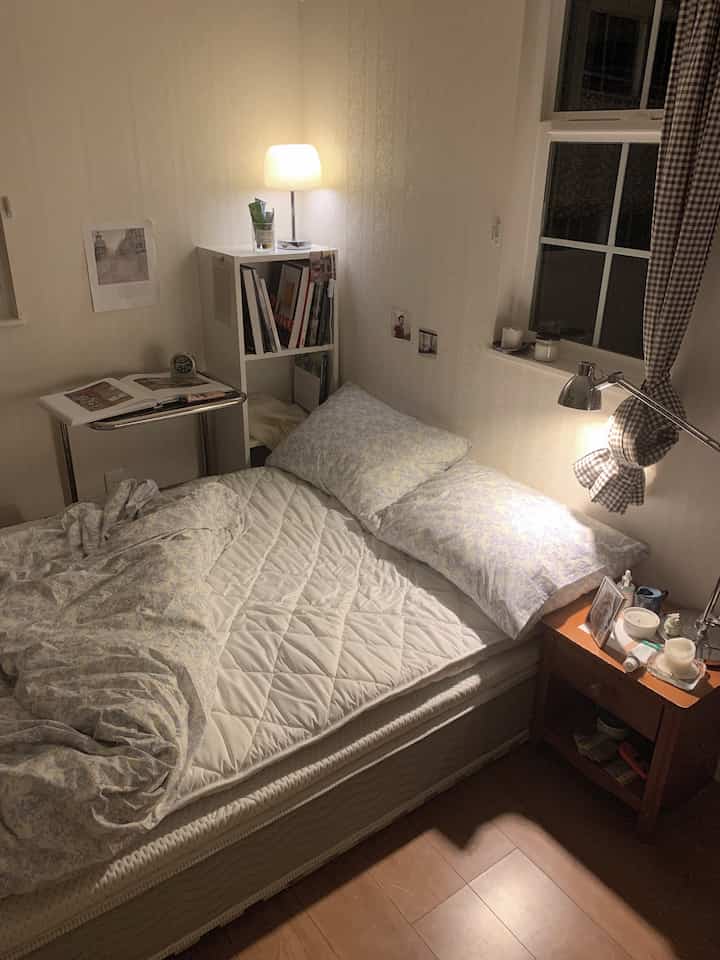 ホワイトの壁と木目調の床がある、ベッドとナイトテーブル、書棚を配したコンパクトな印象的な寝室