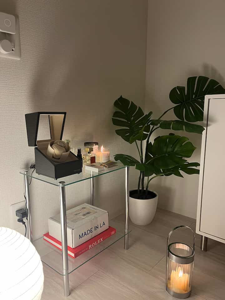 White and natural toned living room corner featuring a glass table with watch winder and candles in a modern setting