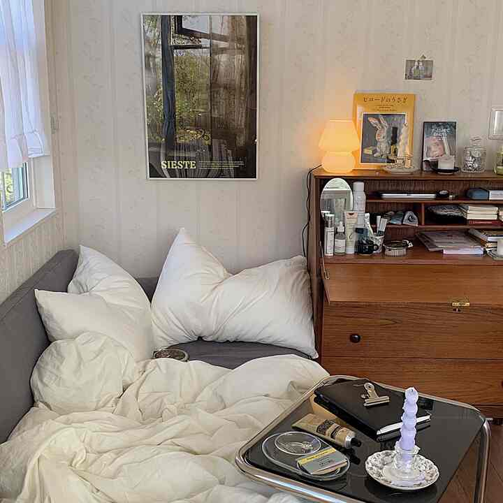 ホワイトとグレーのトーンのコンパクトな寝室、ソファベッドと木製のチェストが配置された落ち着いた雰囲気のインテリア