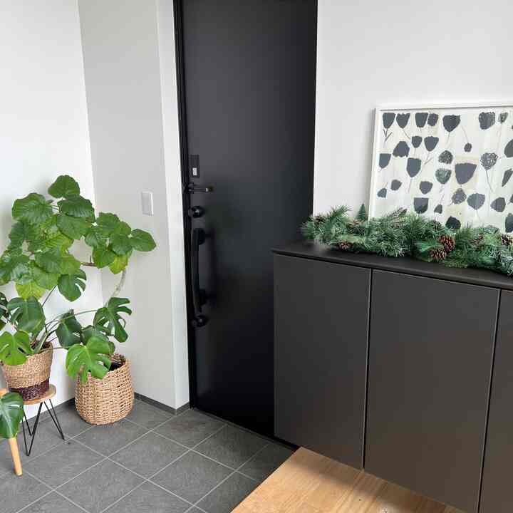 黒いドアとダークな靴箱が配置されたすっきりした玄関、上にはクリスマスのガーランドと緑の植物が飾られた雰囲気のあるインテリア