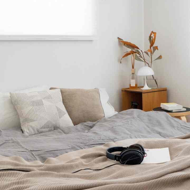 Natural-toned bedroom featuring beige and gray bedding with wooden nightstand, creating a simple and cozy atmosphere