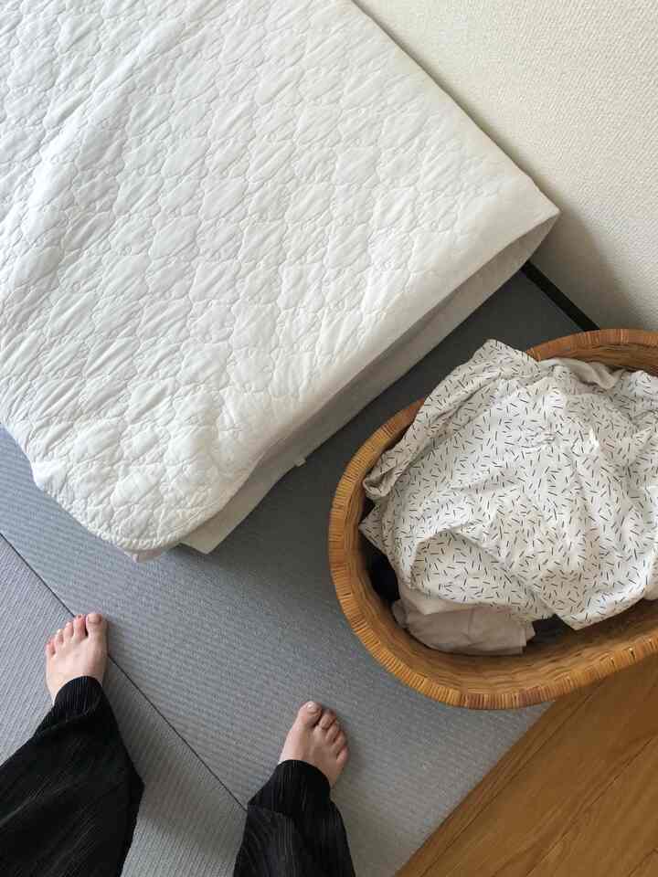 グレーの床マットと木製の床、洗濯かごと白いブランケットが置かれた落ち着いたコンパクトな室内