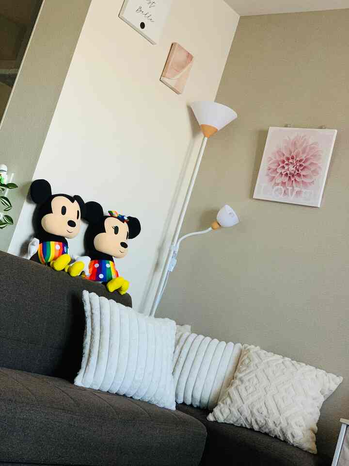 ホワイトとブラウンのトーンの1LDKリビング、ミッキーとミニーのぬいぐるみとフロアランプが配置された印象的な空間