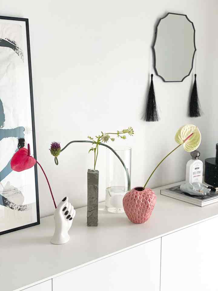 白い背景とサイドボードの上に独特な花瓶と手の形のオブジェが配置されたモダンでミニマルなリビングインテリア