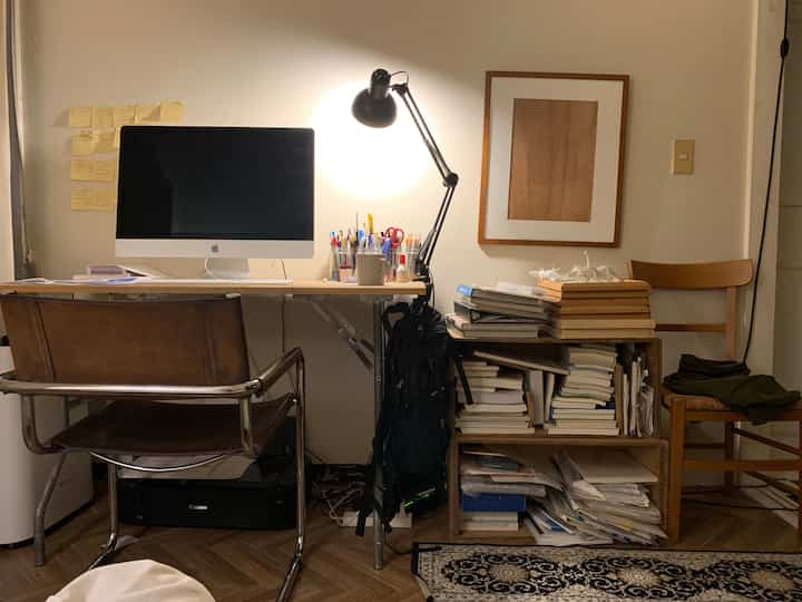 White and wood-toned cluttered home office space featuring desk, bookshelf, and remote work setup