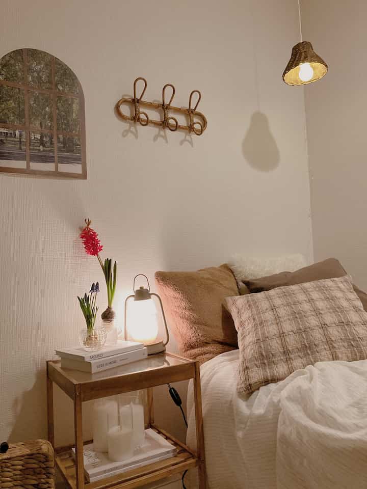 ベージュとブラウン調の寝室、ラタンのペンダントライトと壁掛け、クッションとナイトスタンドが配置された居心地の良いインテリア