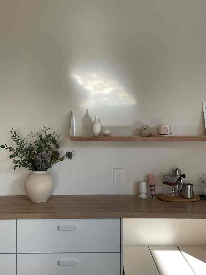 ブラウンの木目調と白を基調としたキッチン空間、植物の入った花瓶とおうちカフェグッズが整然と配置されたミニマルなインテリア