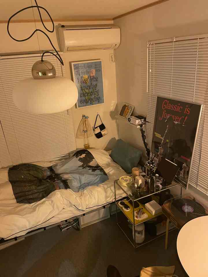 ホワイトが基調のワンルーム寝室、ヴィンテージポスターとペンダントライトが配置された落ち着いた空間