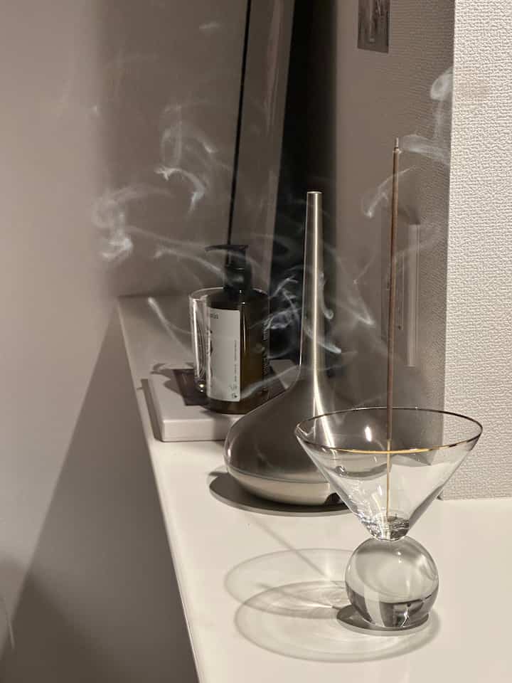 Minimal interior corner featuring a silver diffuser and a transparent glass incense holder with subtle smoke rising