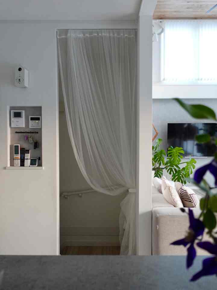 白とベージュのトーンのリビング、透明なカーテンと植物が配置されたモダンでナチュラルなインテリア
