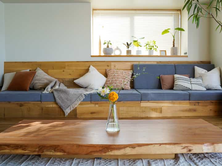 ナチュラルな色調のリビング、低めの木製テーブルと木目調のベンチソファが配置された雰囲気のある空間