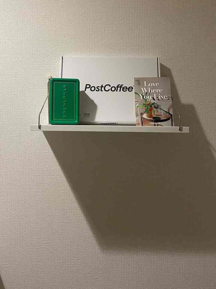 Minimal interior with a small shelf mounted on white wall holding a green tin box, white PostCoffee package, and a booklet in cafe style setting