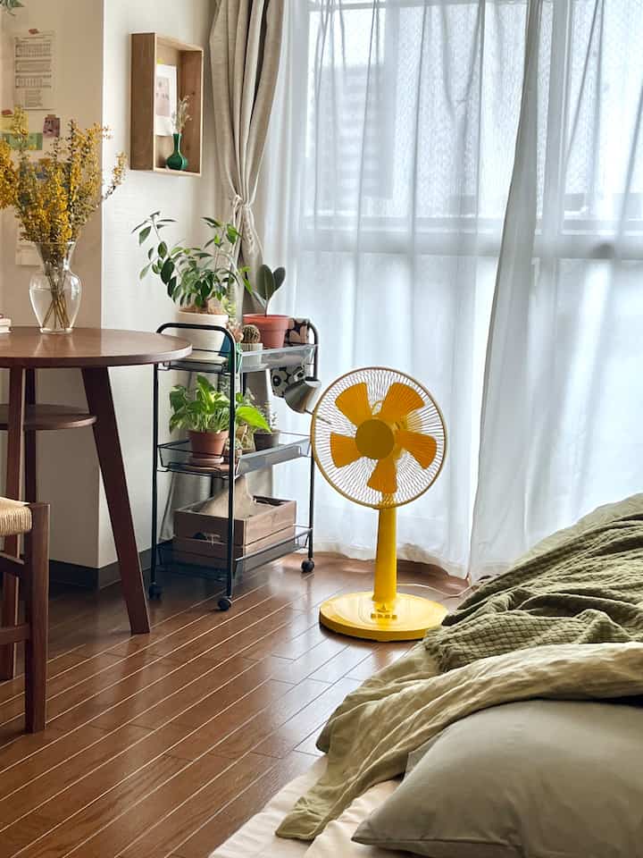 Natural modern living room with wood tone flooring and a yellow fan near a veranda covered by sheer curtains