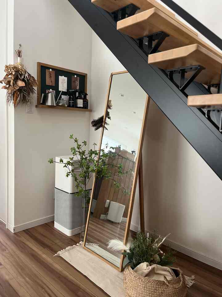 Natural wood tones and white walls define a living space under stairs, featuring a large floor mirror and a woven basket for storage in a clean interior