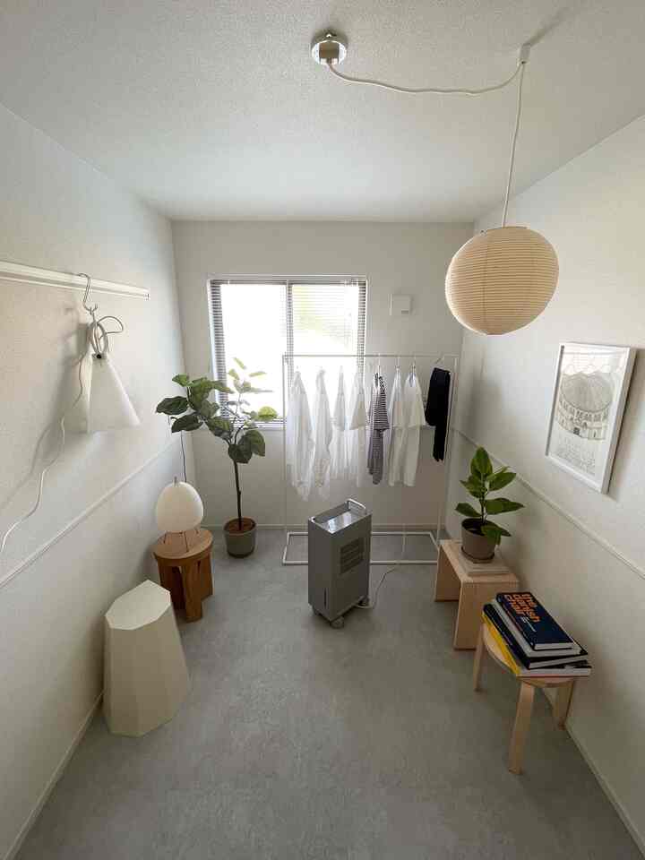 明るいホワイトとグレーのトーンのコンパクトな狭い部屋、中央にハンガーラックとペンダントライト、植物が配置されたシンプルなインテリア