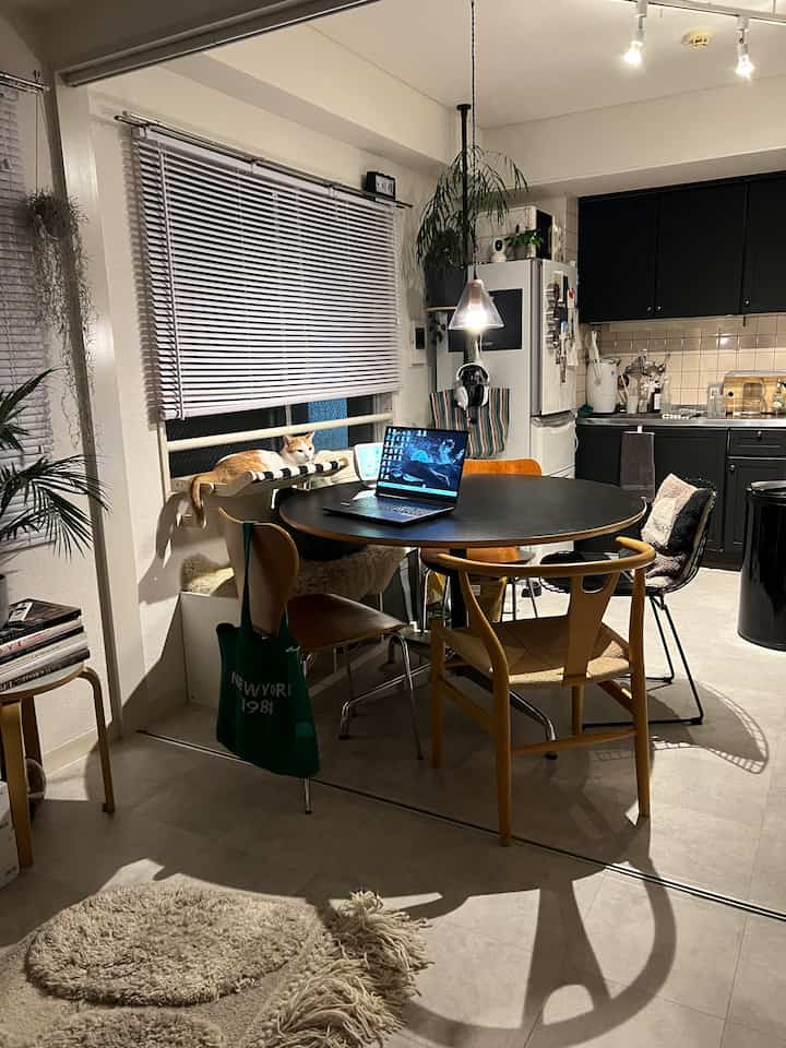 Natural-toned dining room featuring a round dining table with four chairs, a cat relaxing on a cat tower by the window, creating a cozy atmosphere