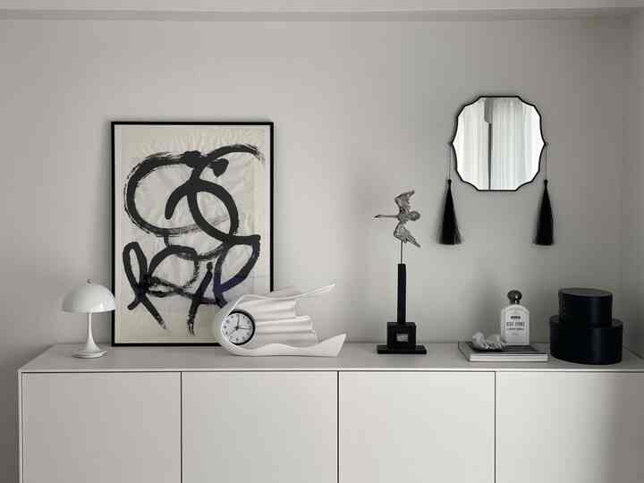 白と黒の調和が美しいモノトーンインテリア、額縁や鏡、テーブルランプが配置されたシンプルな空間