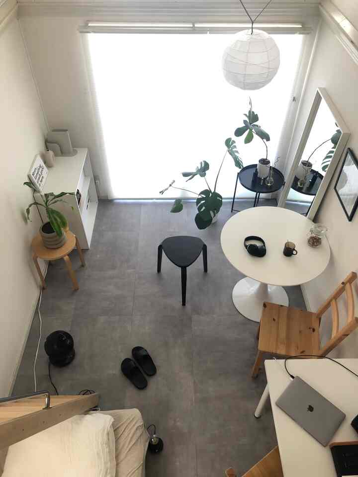 Bright white and gray studio loft featuring a compact bed, desk with laptop, round dining table, and green plants in a modern setting