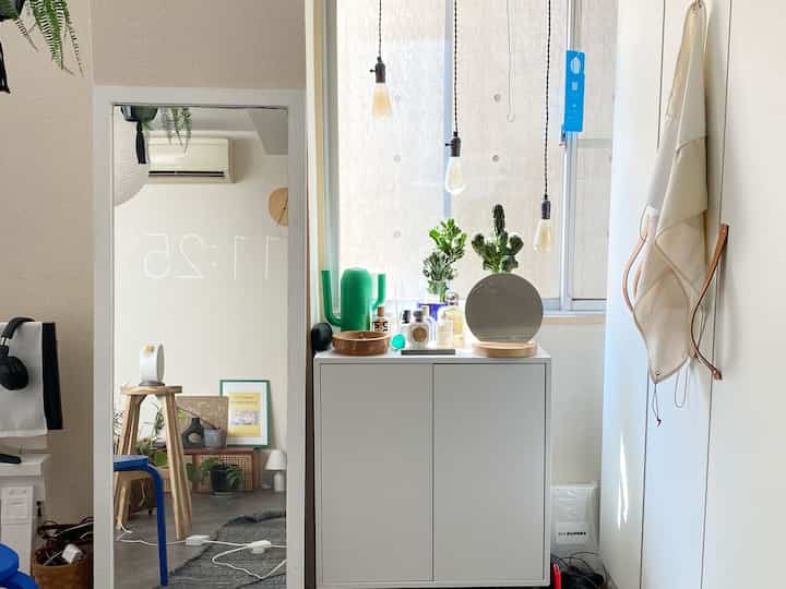 白を基調とした小さな部屋、窓際に置かれた白いキャビネットの上にサボテンや様々な装飾品が配置されたミニマルで清潔感のあるインテリア