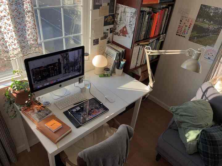 White-toned home office with desk and computer near window, bookshelf and diverse wall posters creating a cozy workspace