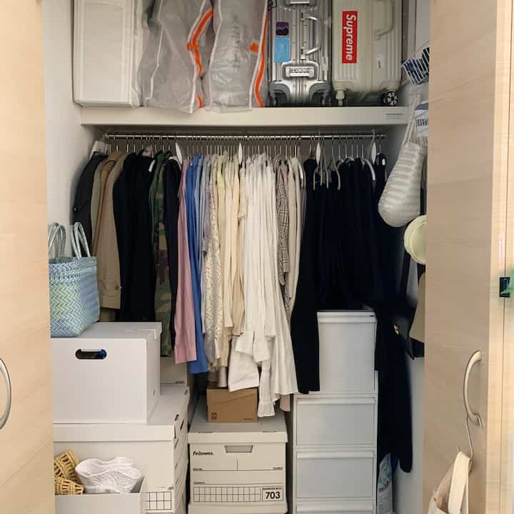 白とベージュのトーンのクローゼット、整理された収納箱とハンガーに掛けられた衣類が配置されたコンパクトで清潔な空間