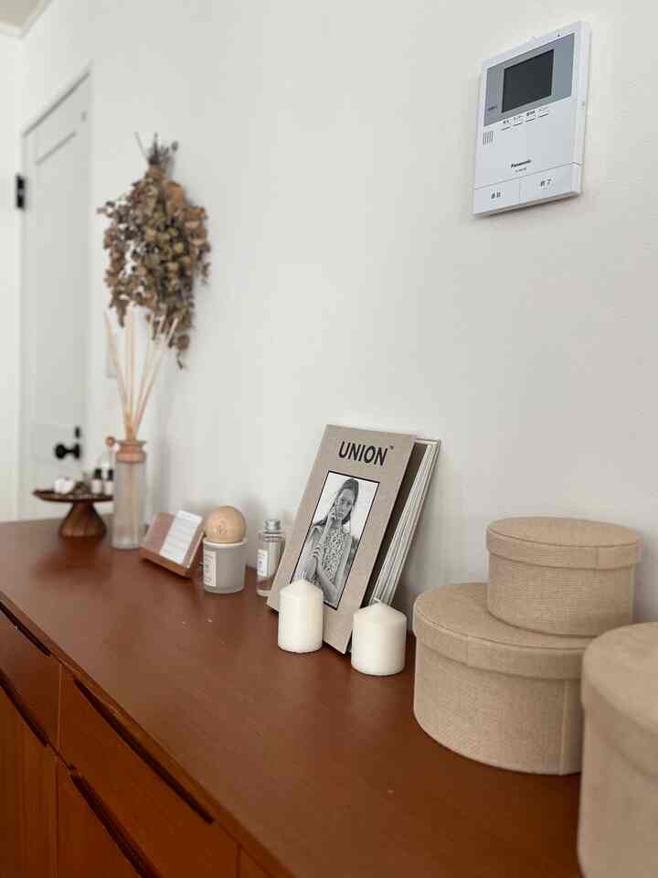 白い壁と茶色の木製収納が配置されたナチュラルな雰囲気のインテリア、キャンドルや額装アートなどの装飾が印象的な空間