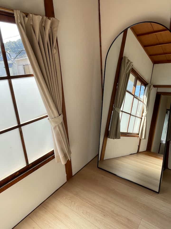 Beige curtains and wood tones feature in an old folk house style room with a full-length mirror, creating a natural atmosphere
