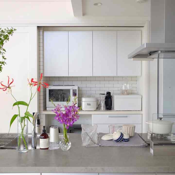 白を基調としたシンプルなキッチン空間。タイルのバックスプラッシュと調理家電、花瓶が配置された雰囲気のあるインテリア