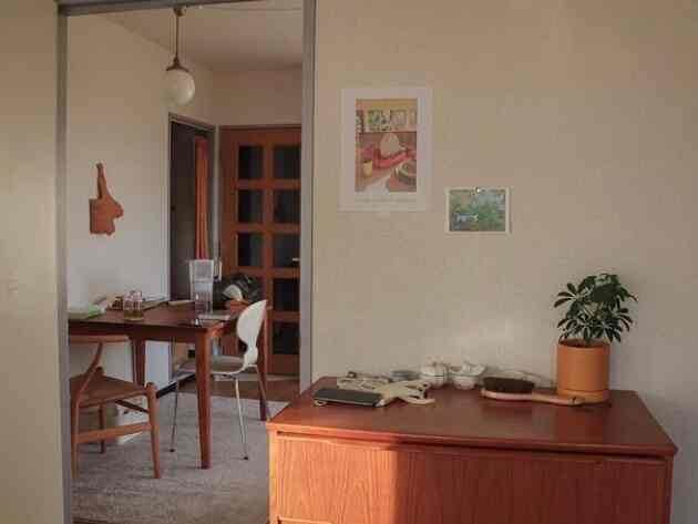 Beige walled studio apartment featuring brown wooden furniture, dining table and chairs, indoor plant, and picture frames creating a natural atmosphere