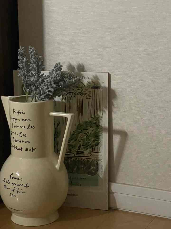 ベージュ色の花瓶と額縁が木製の床とベージュの壁の前に配置された、ナチュラルな雰囲気のインテリア