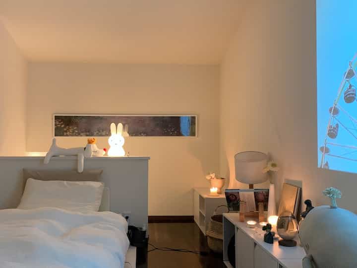 ホワイトとベージュのトーンのミニマルな寝室、ベッドとテーブルランプ、キャンドルが配された雰囲気のあるインテリア