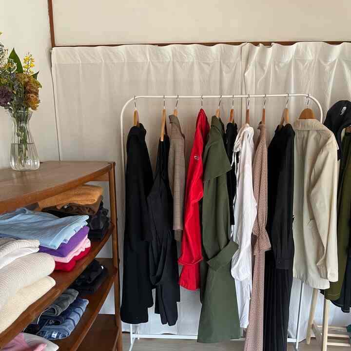 White backdrop and wooden shelf with a clothing rack featuring various colored garments in a neat closet area