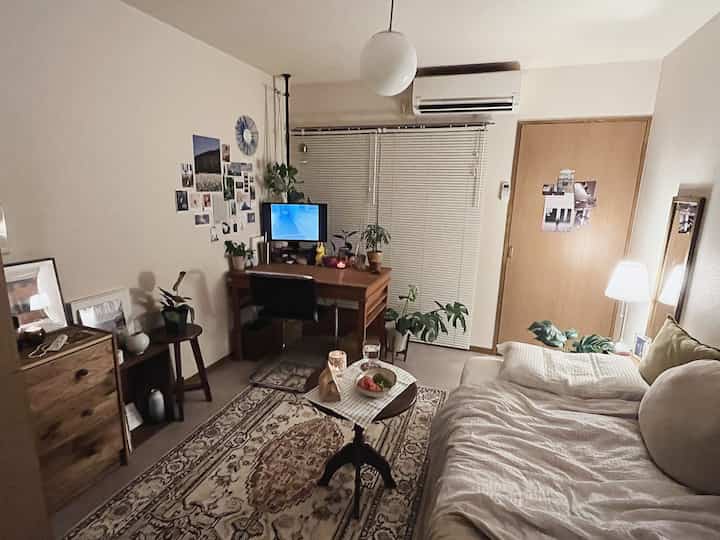 White and brown toned bedroom with a compact space featuring a bed, desk, rug, and plants in a cozy home office setup