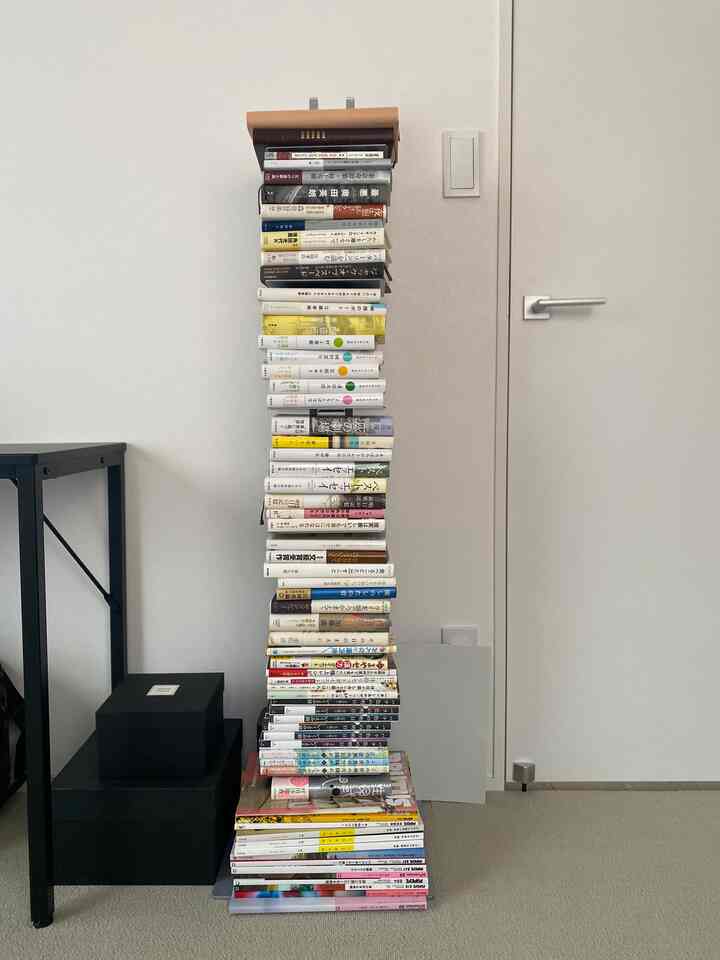 白い壁とクローゼットが背景のウォークインクローゼットに中央に高く積まれた本の塔と左側の黒い収納箱が配置された雰囲気のある空間