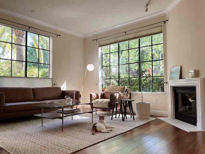 Beige-toned living room featuring brown leather sofa and armchair, coffee table with a cat resting comfortably, natural rustic atmosphere