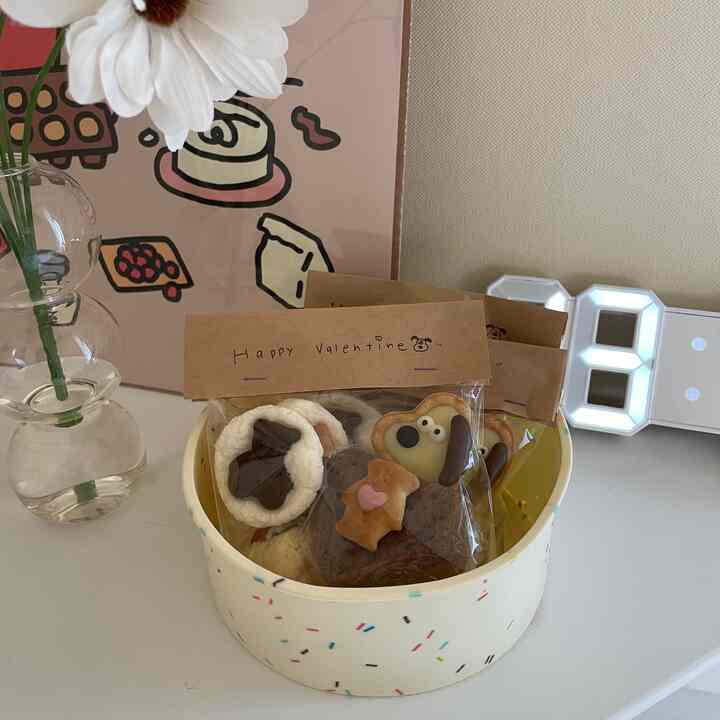 白と茶色の色調のキッチンテーブルに花瓶、ベーキングポスター、バレンタインデーのクッキーボックスが配置された雰囲気のある空間