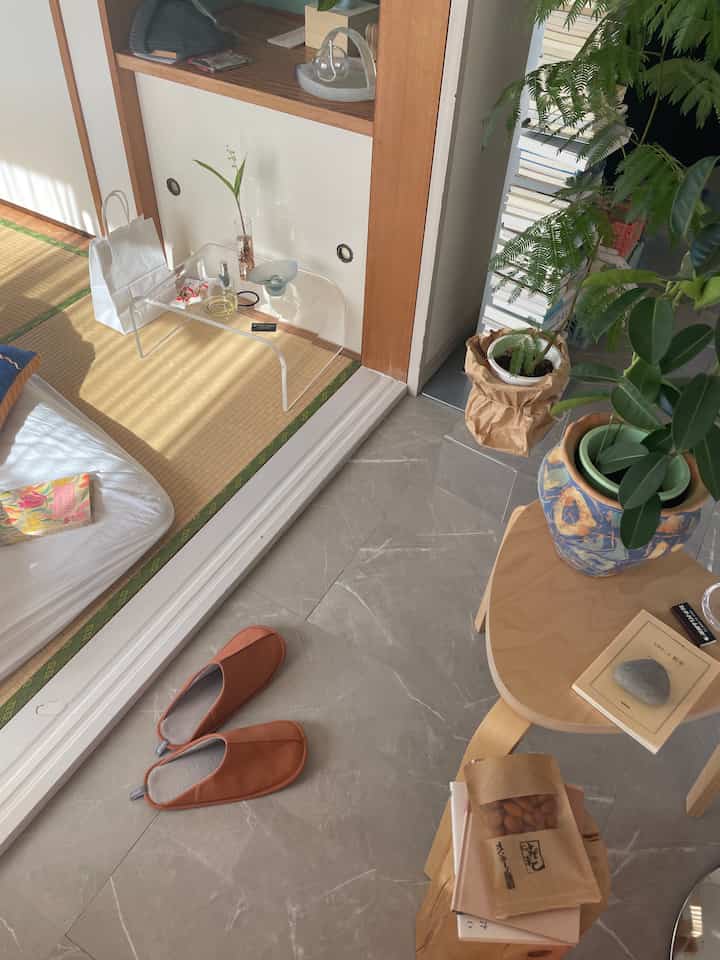 A natural color and wood tone living space featuring tatami mats, a clear acrylic table, natural plants, and a stool arranged in a relaxed Japanese style interior