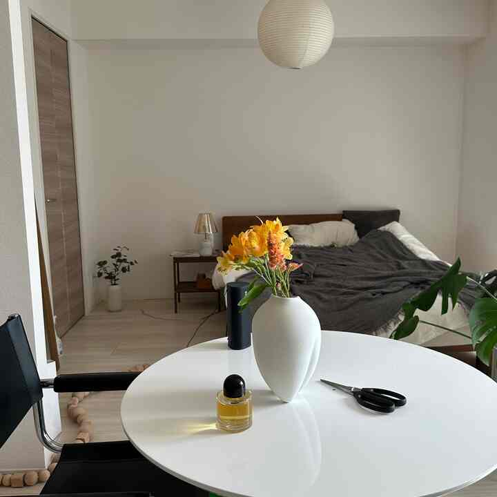 A white and brown toned studio bedroom and dining area featuring a round table with flowers and a wooden bed creating a natural modern vibe