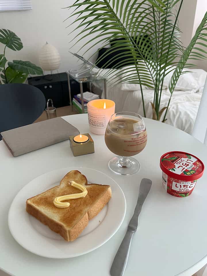 White and natural colors blend in a bedroom interior, cozy home cafe setting with coffee glass, toast, and candles on dining table