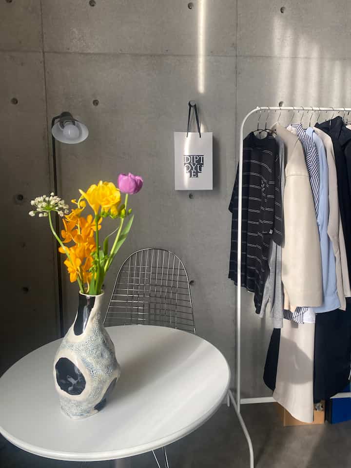 明るいグレーのコンクリート壁と白いラウンドカフェテーブルに春の花が飾られたミニマルなワンルームインテリア