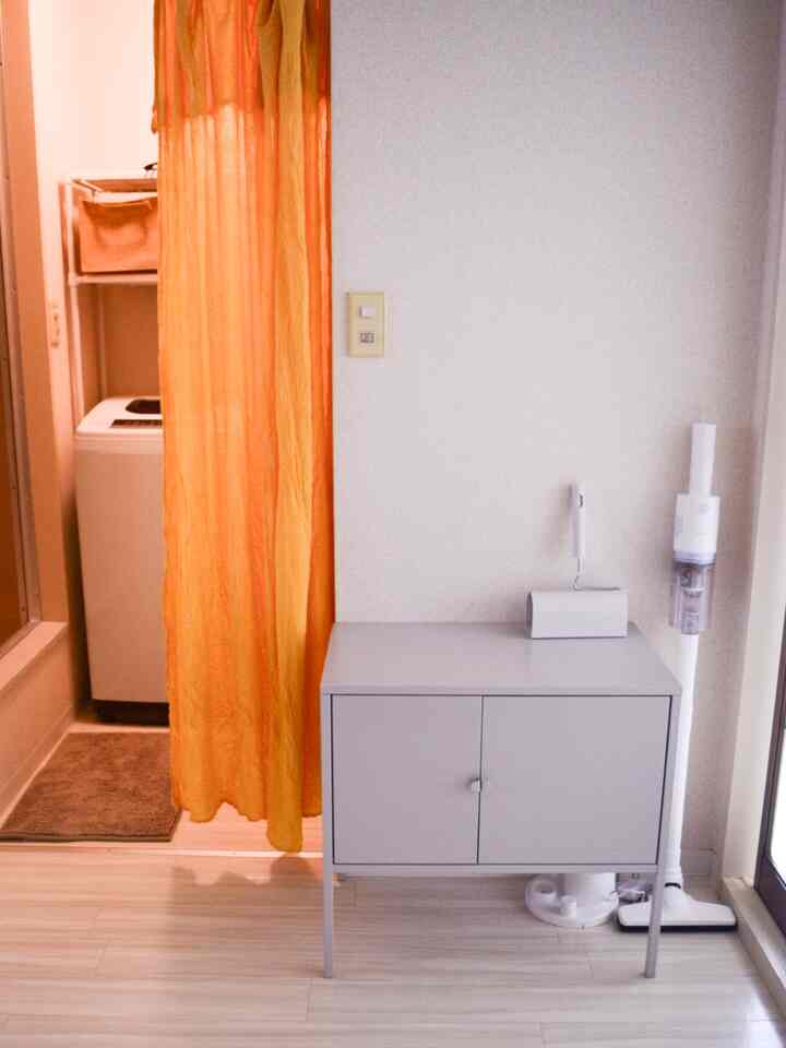 ホワイトの壁と床にオレンジのカーテンがアクセントの、洗濯室と収納キャビネットがあるモダンな空間