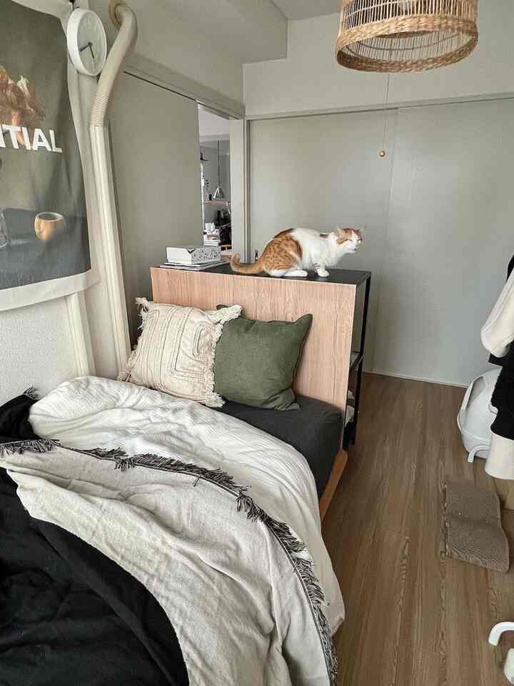 White and brown toned bedroom featuring a wooden bed with cushions and a woven pendant light, creating a cozy atmosphere