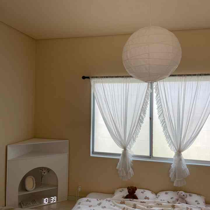 柔らかなベージュの壁と白い寝具、窓のカーテンが配置された落ち着いた寝室のインテリア