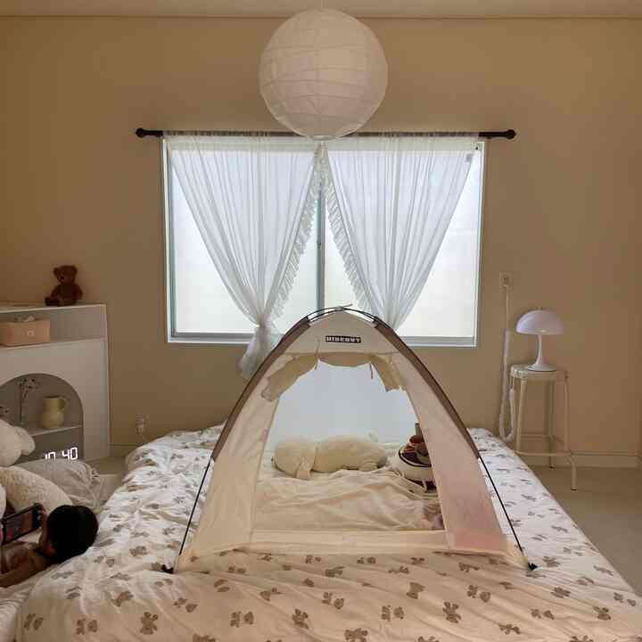 白とベージュの色調の寝室、中央に子供用テントが置かれたベッドとリラックスする子供がいる、雰囲気のある空間