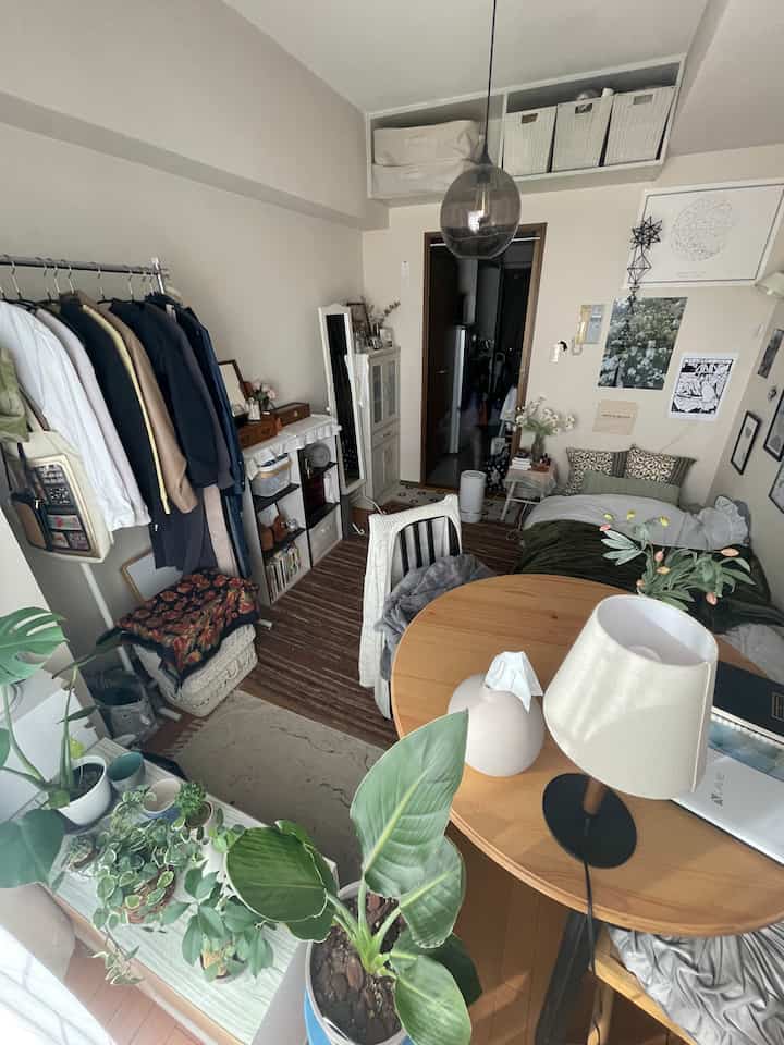Natural brown-toned single-occupant studio apartment featuring round dining table, bed, and various plants creating cozy atmosphere