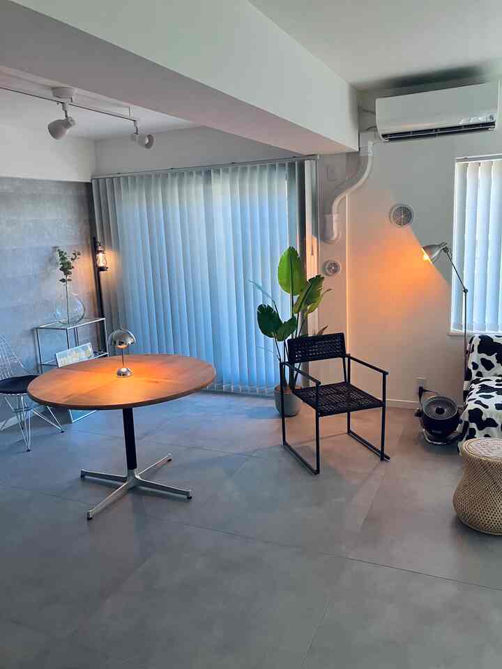 グレーの床とナチュラルモダンスタイルのダイニングルーム、丸いダイニングテーブルとメタルチェア、ブラインドが配置されたシンプルな空間