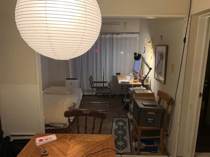 ナチュラルな木目調のワンルーム、ベッドとホームオフィス用のデスクが配置された落ち着いた空間