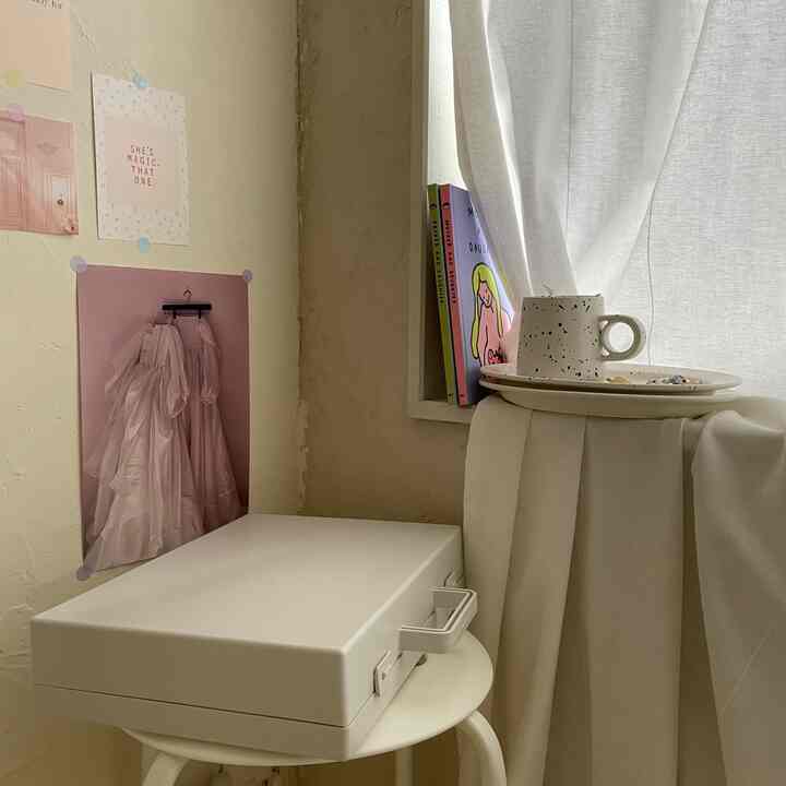 A cozy small space in white and beige tones featuring a carry case and stool with cup and candle placed near the window