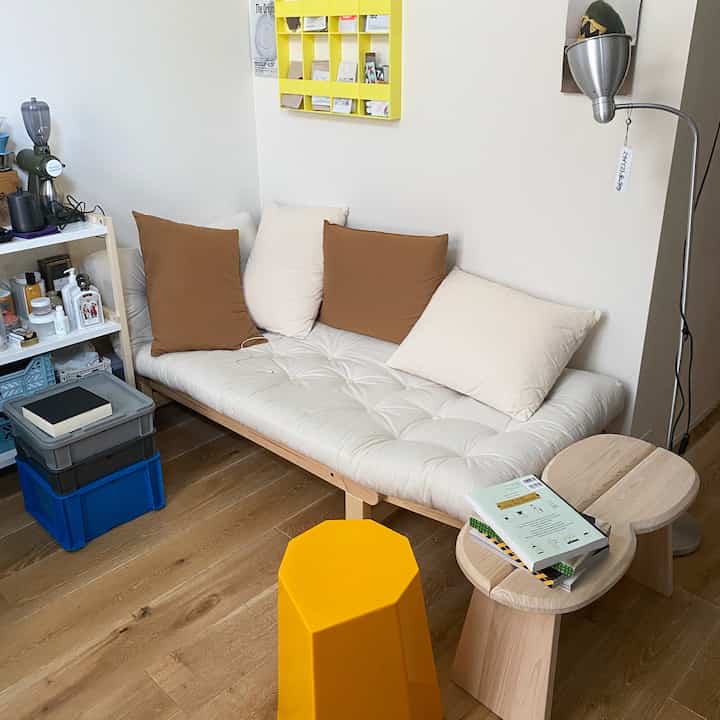White sofa bed with wood tone flooring and yellow stool in a cozy single household living room