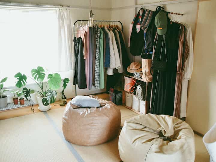 白とベージュの自然な色調の6畳の畳の部屋、ビーズクッションやハンガーラック、植物が配置された落ち着いた雰囲気の空間